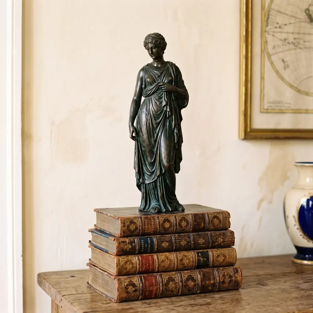Bronze classical statue beside a stack of antique leather books
